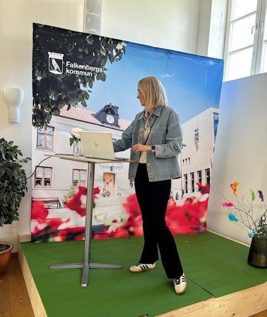 En blond kvinna står vid ett ståbord på en scen och tittar ner på en dator.