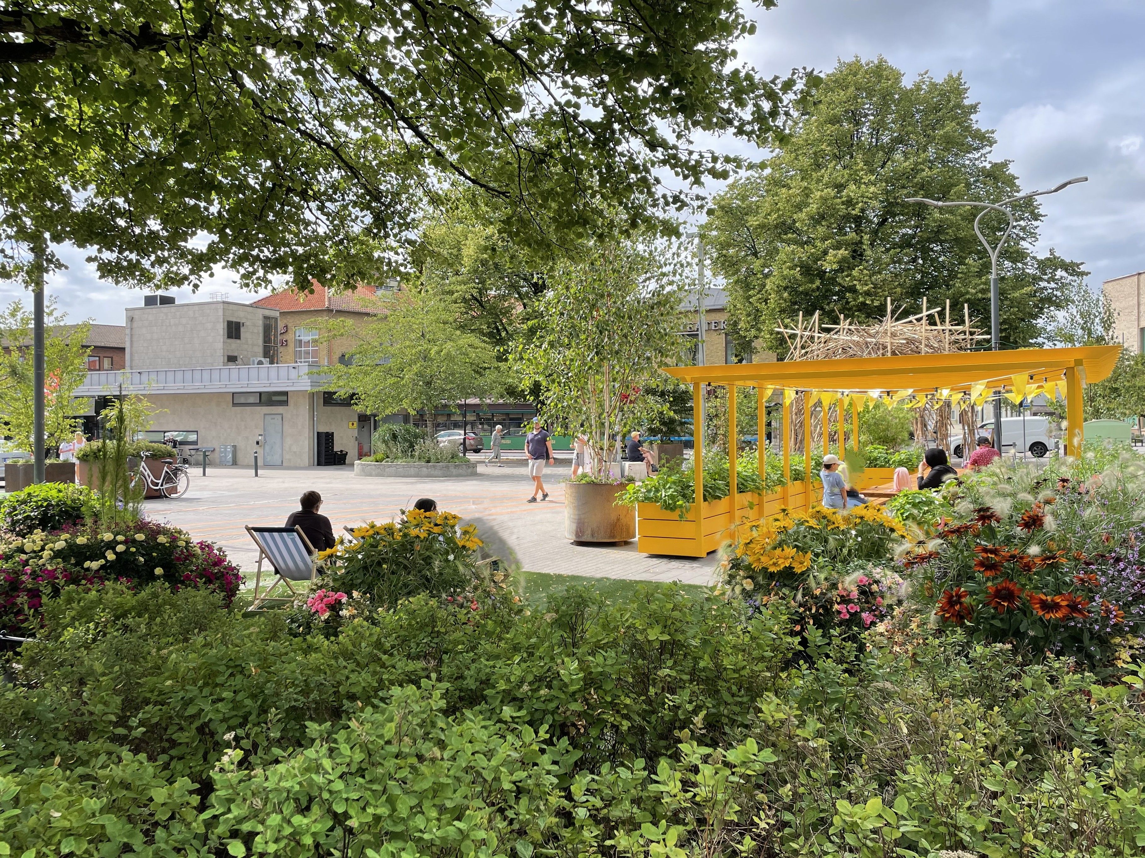 Blomstrande rabatt, person i solstol, pergola i gult.