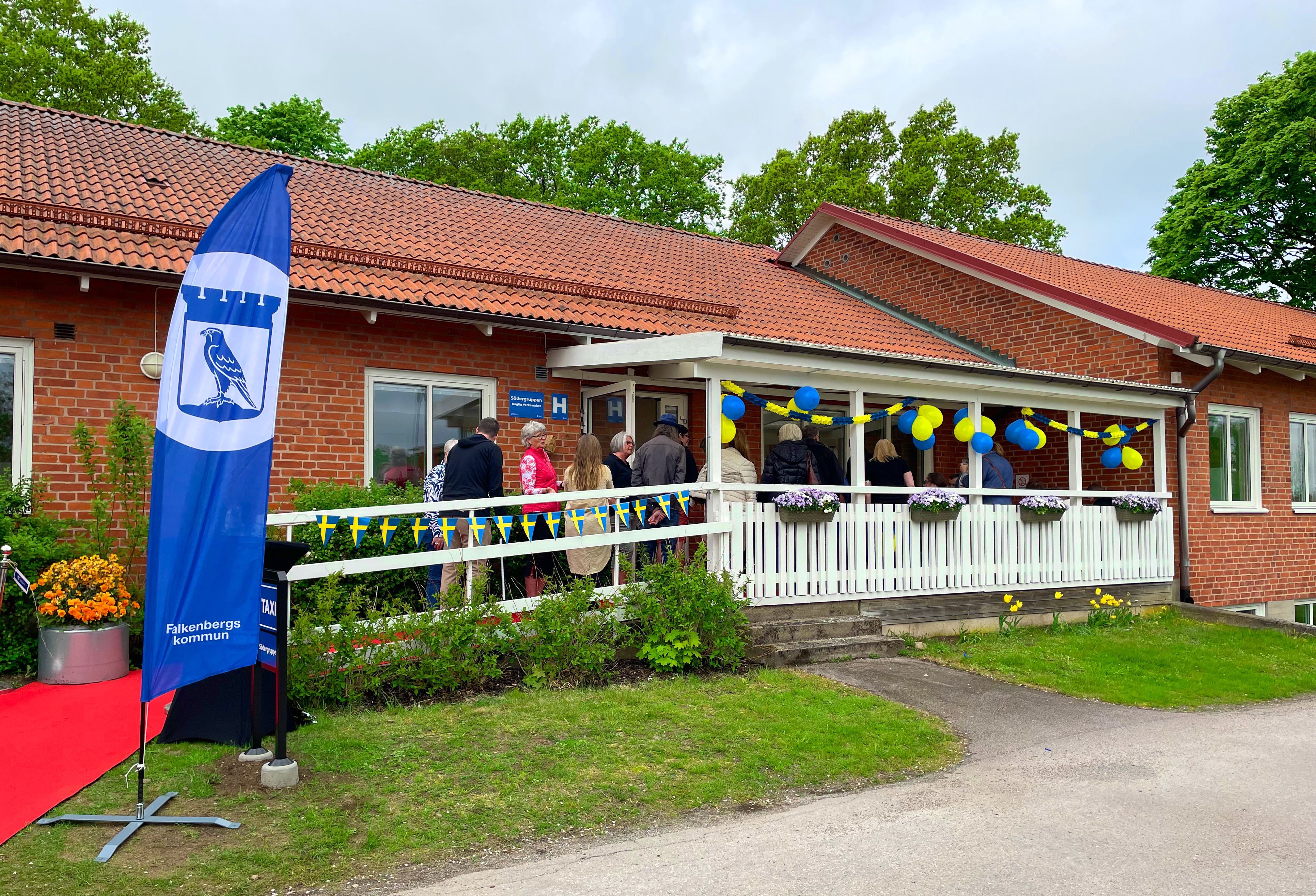 Södergruppens entré, flera personer står i kö för att få komma in. I förgrunden syns en blå flagga med Falkenbergs logotyp.