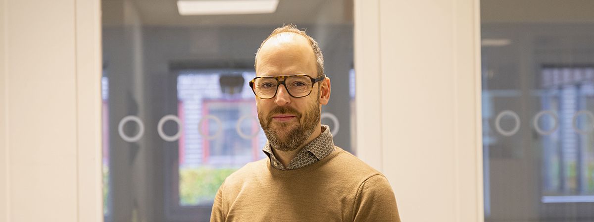 Philipp Seuffer har skägg och glasögon. Han står inomhus och ler något.