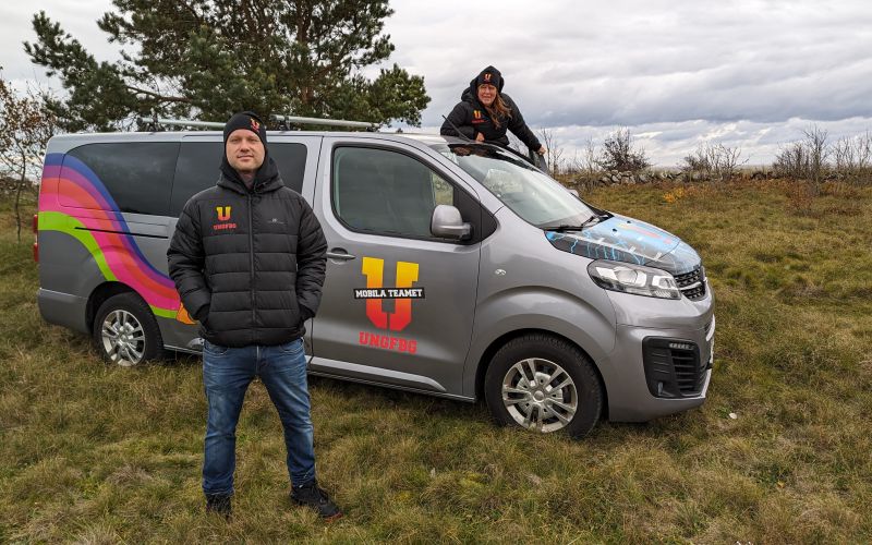 En man framför minibuss med texten Mobila teamet - Ung Fbg. Vid förardörren bakom minibussen syns en kvinna.