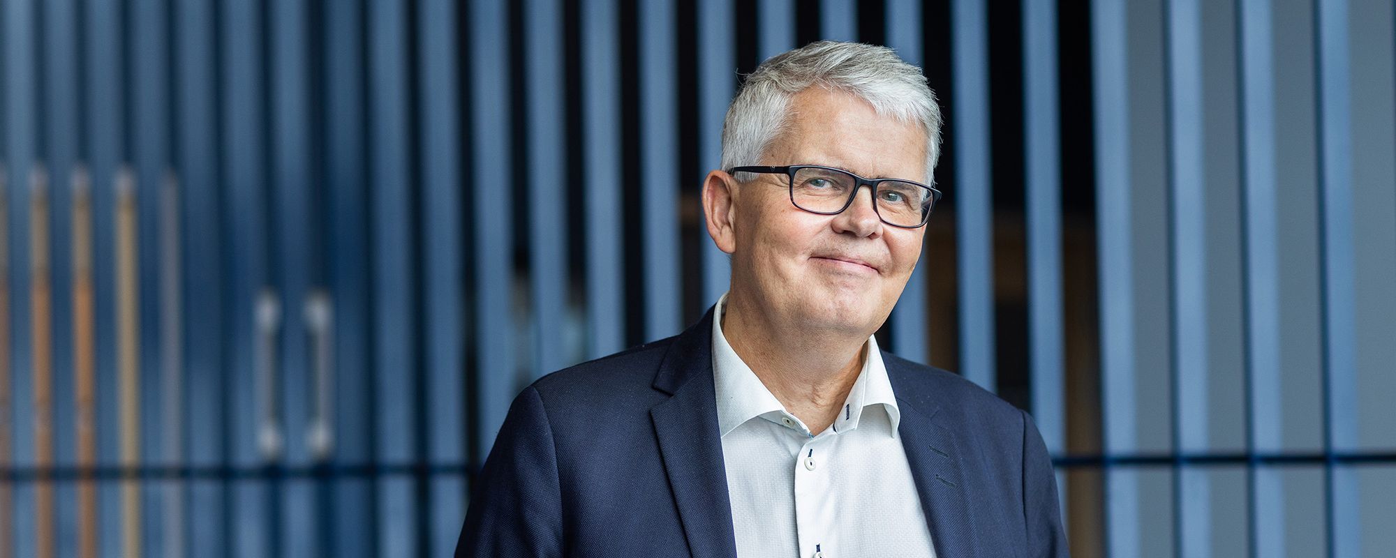 Henrik Petzäll framför en lamellgardin. Han ler.