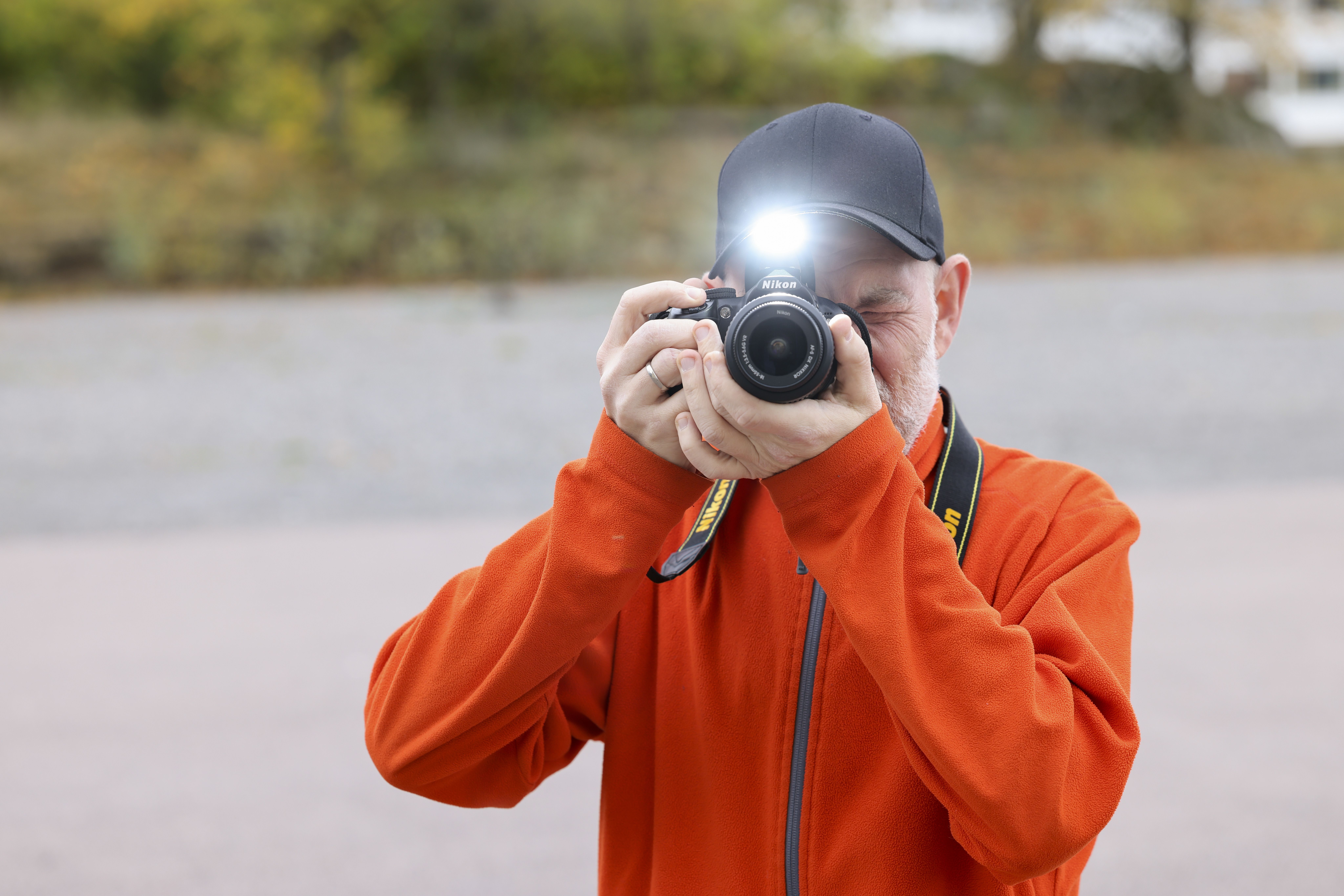 En man i orange fleecetröja fotograferar rakt framifrån, blixten är på.