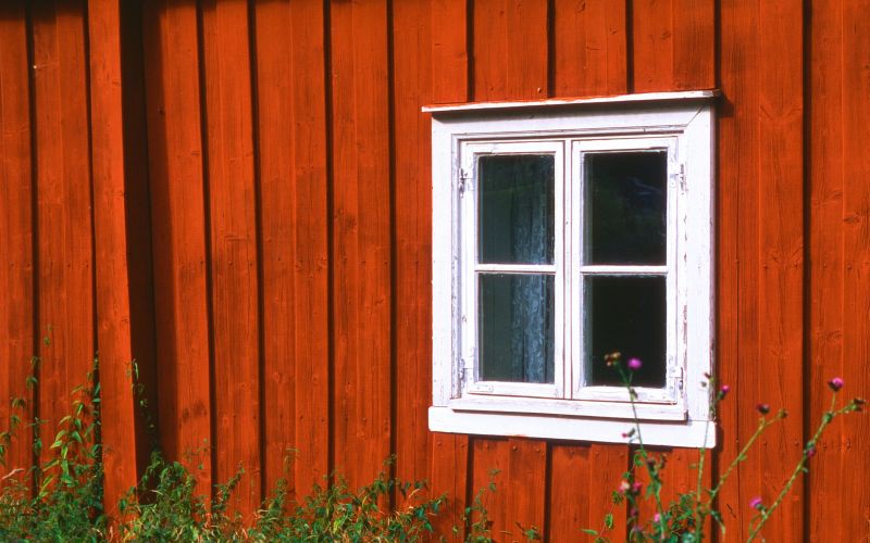 Röd träfasad och ett vitt fyrkantigt fönster.
