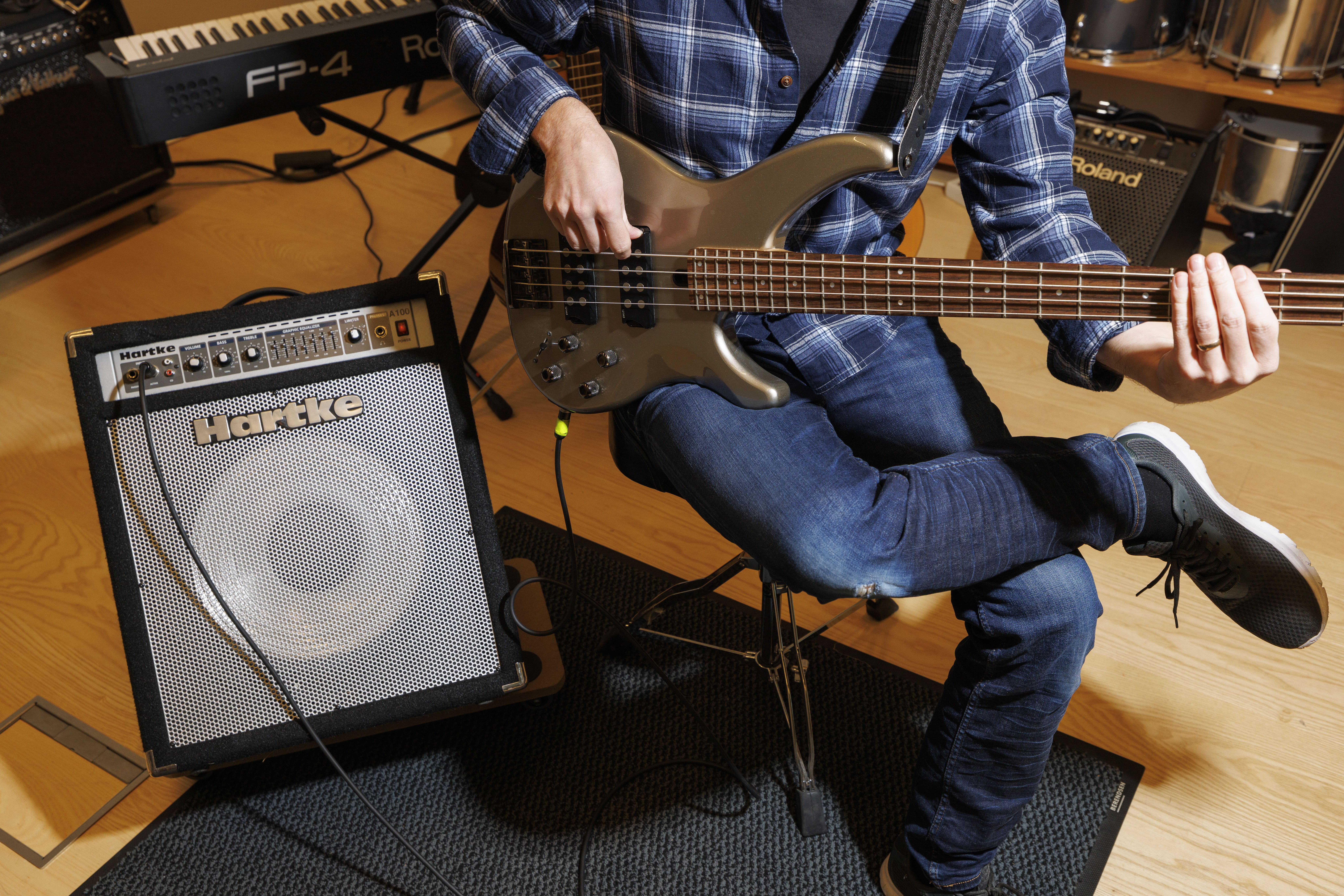 En person i rutig skjorta sitter och spelar elgitarr. Bredvid står en förstärkare