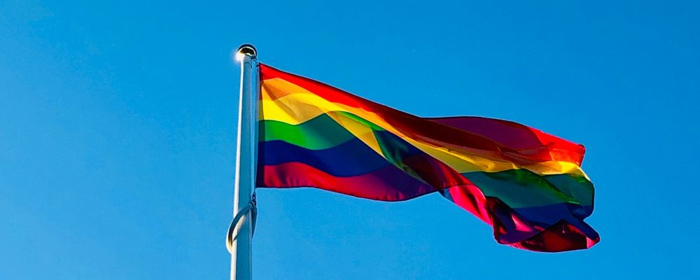 En prideflagga på en stång mot en blå himmel.