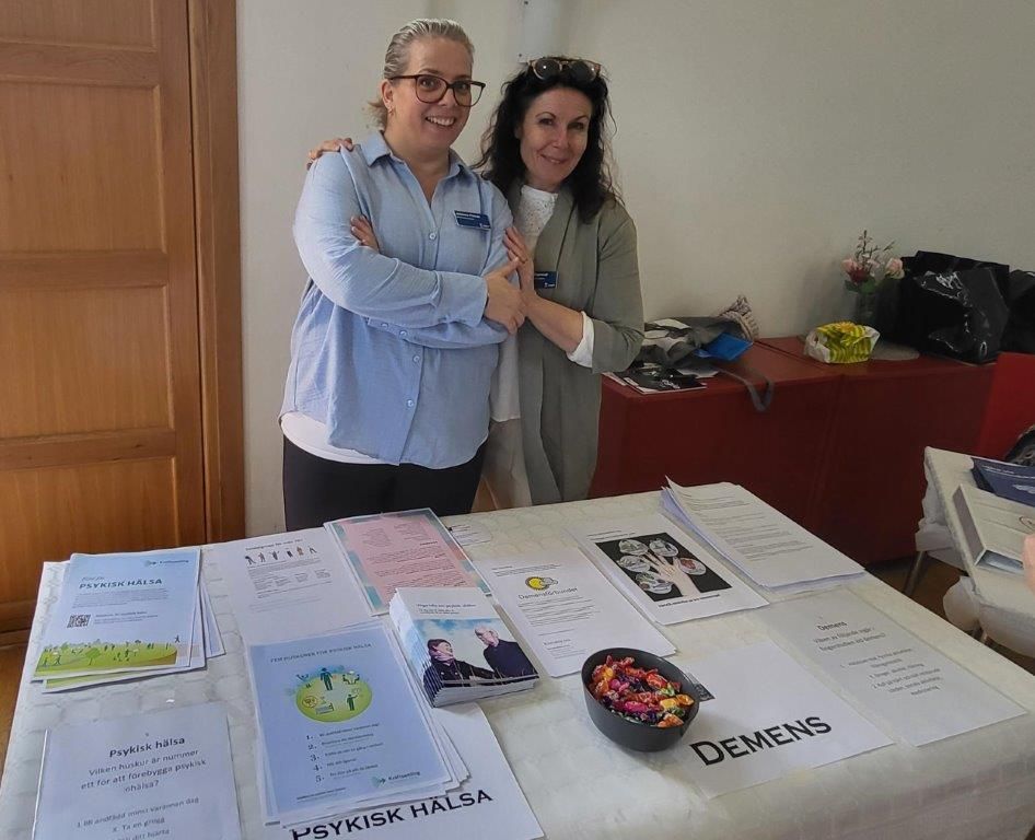 Två kvinnor står bakom ett bord fyllt med informationsmaterial.