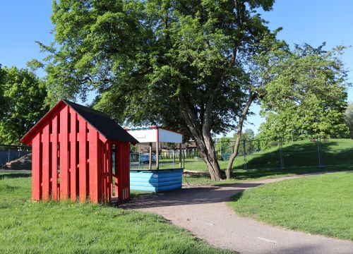 Miniväg med gräs på båda sidor, några träd, en kiosk och en röd stuga