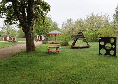 Gräsmatta med trähydda, bord, bänkar och bollkastningsplank