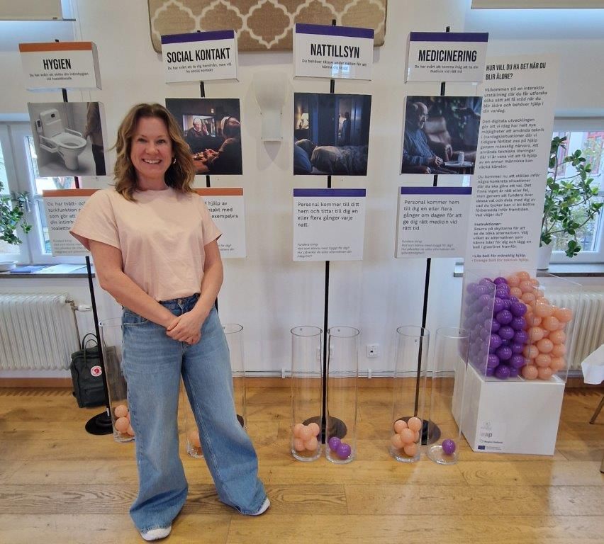 Leende kvinna med brunt hår står framför en rad med informationsskyltar.