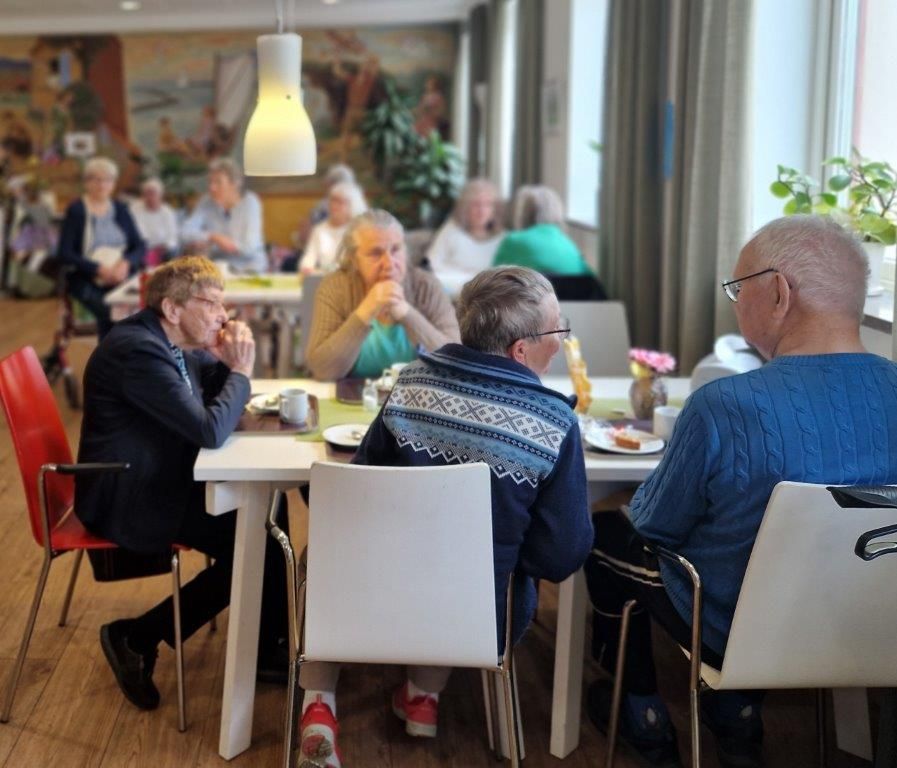 Äldre personer sitter runt ett bord och fikar.