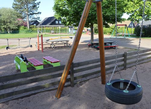 Gunga med leksaksbil, balansorm och bänkar i bakgrunden