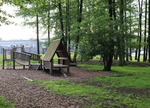 Trähydda och bro i skogstunge med byggnad i bakgrunden