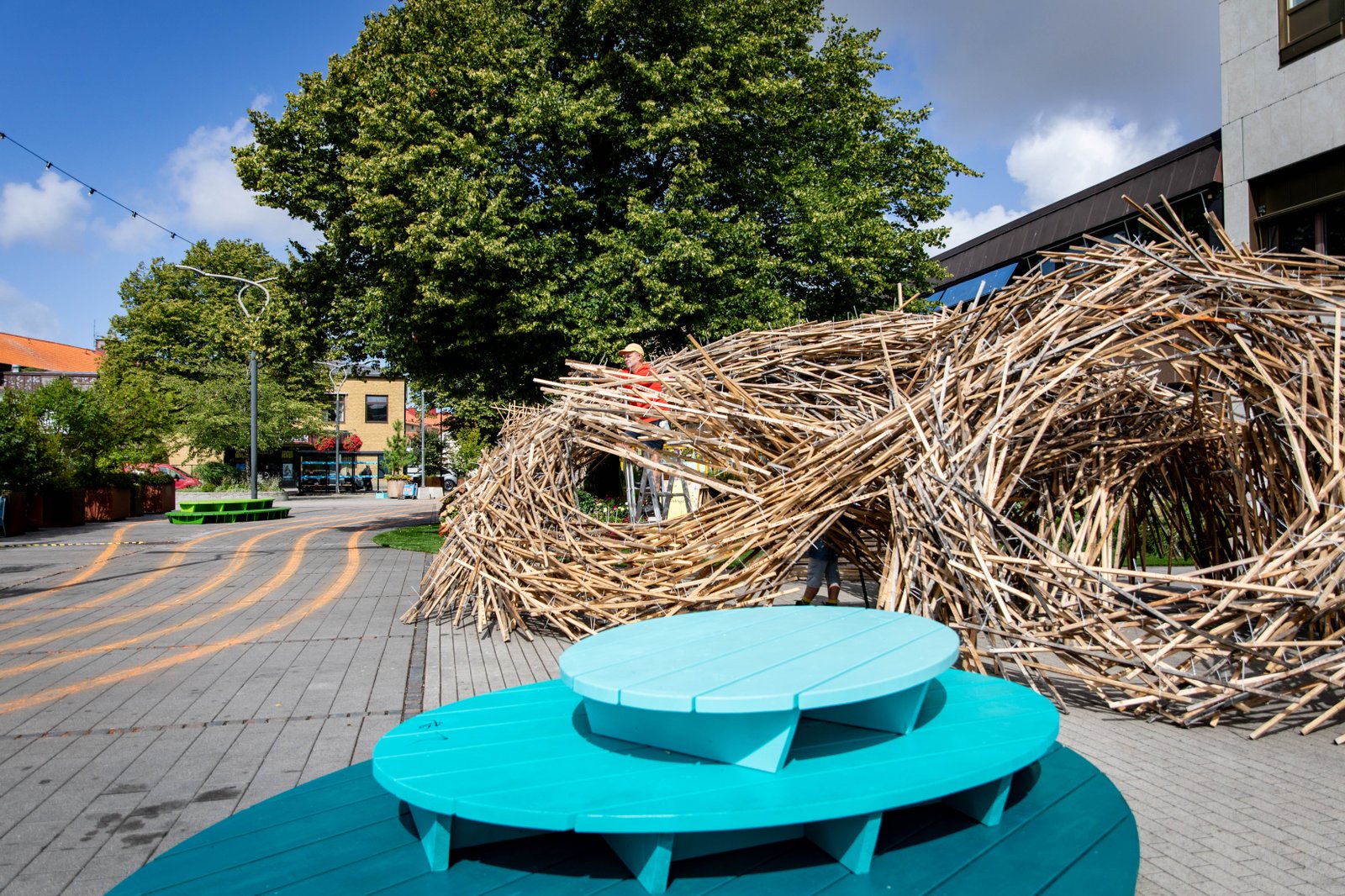 Sommartorg, konstverk av trä i bakgrunden och en turkos sittmöbel i förgrunden.