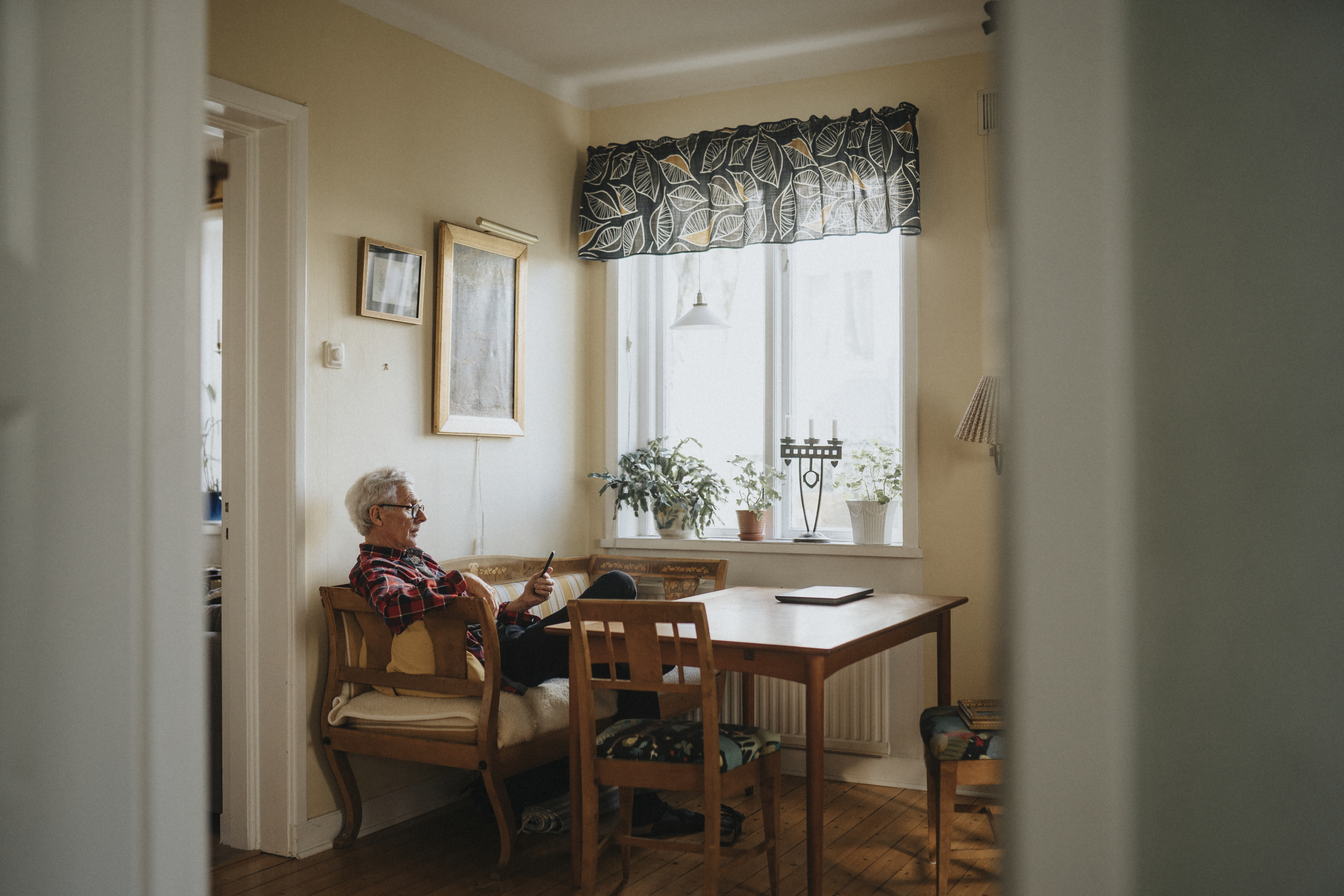 Äldre man med mobiltelefon, sitter på soffa av äldre årsmodell.