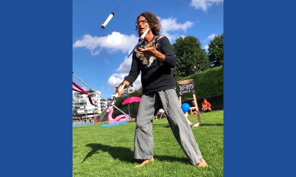 Magnus jonglerar, har röd näsa, och är barfota på en gräsmatta.