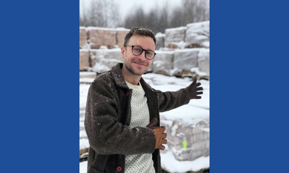 Carl ler in i kameran, står ute i snön vid stora lass med tegel.