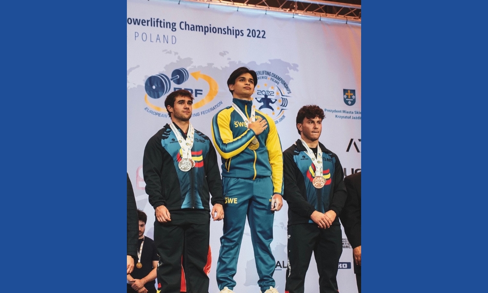 Carl på podium med guldmedalj och hand över bröstet. Silver och bronsmedaljör bredvid.