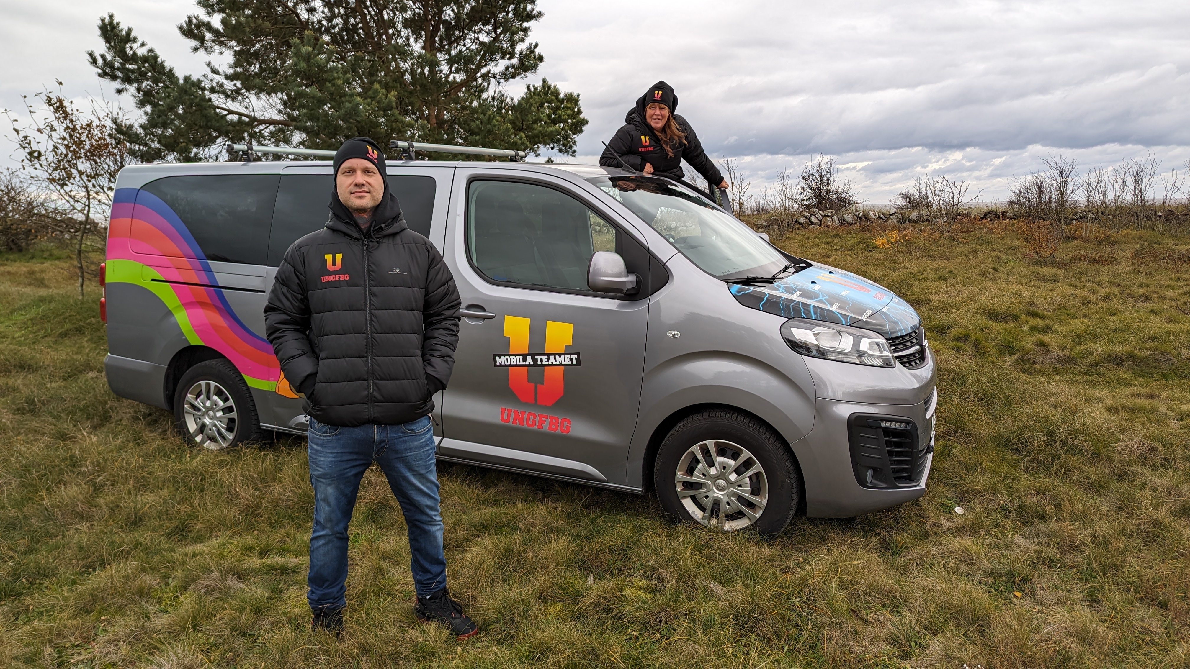 En man framför minibuss med texten Mobila teamet - Ung Fbg. Vid förardörren bakom minibussen syns en kvinna.