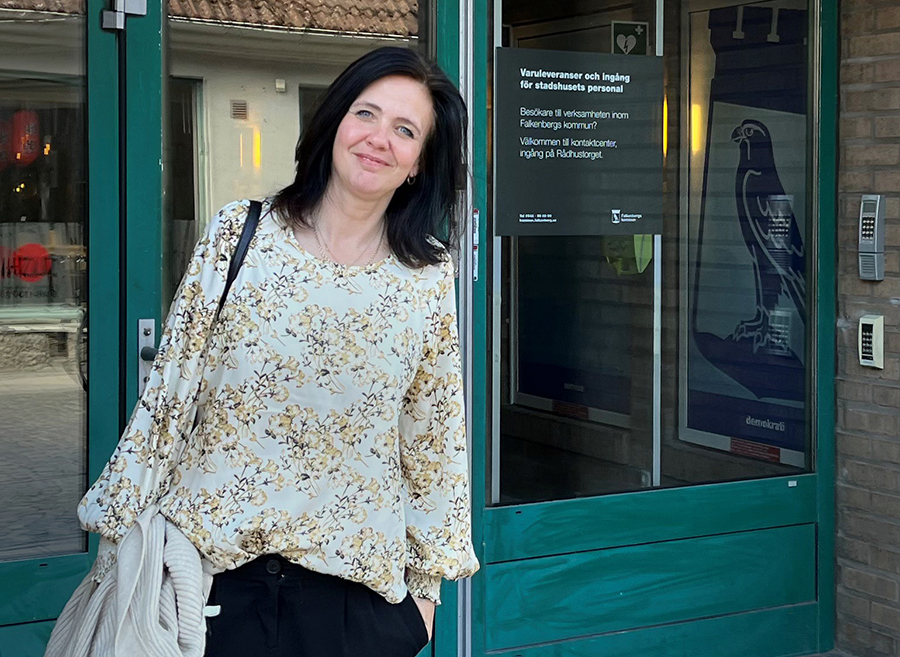 Leende kvinna med axellångt, mörkbrunt hår står utanför en entré.