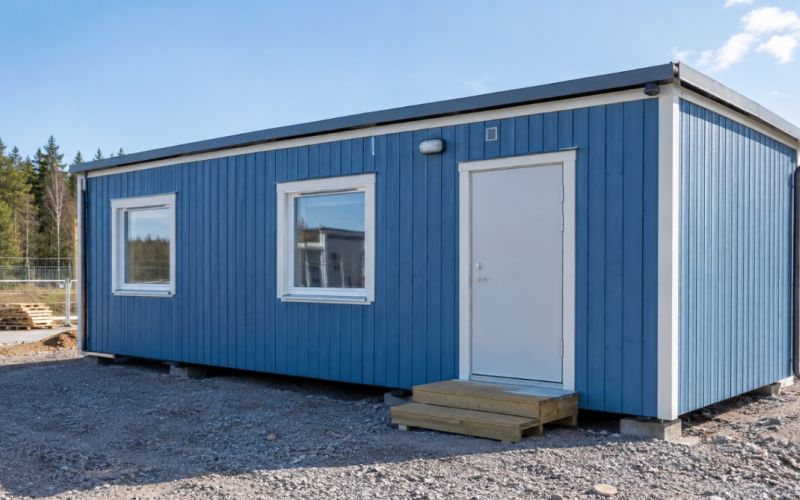 Blå byggbod med vit dörr och vita fönster.
