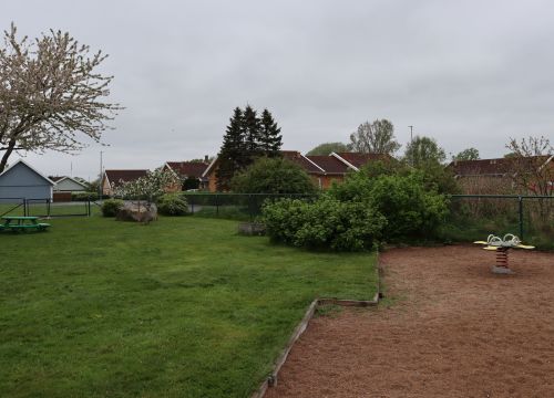 Sandlåda med gungleksak och grön gräsmatta