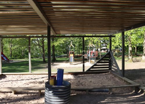 Sandlåda med solskydd – gräsplan och träd i bakgrunden