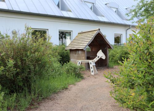 Vit trähäst och liten stuga i slutet av grusgång, buskar på sidorna