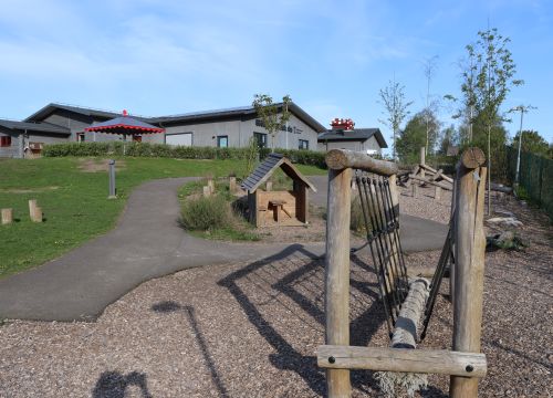 Balansbana med lekstuga och förskola i bakgrunden