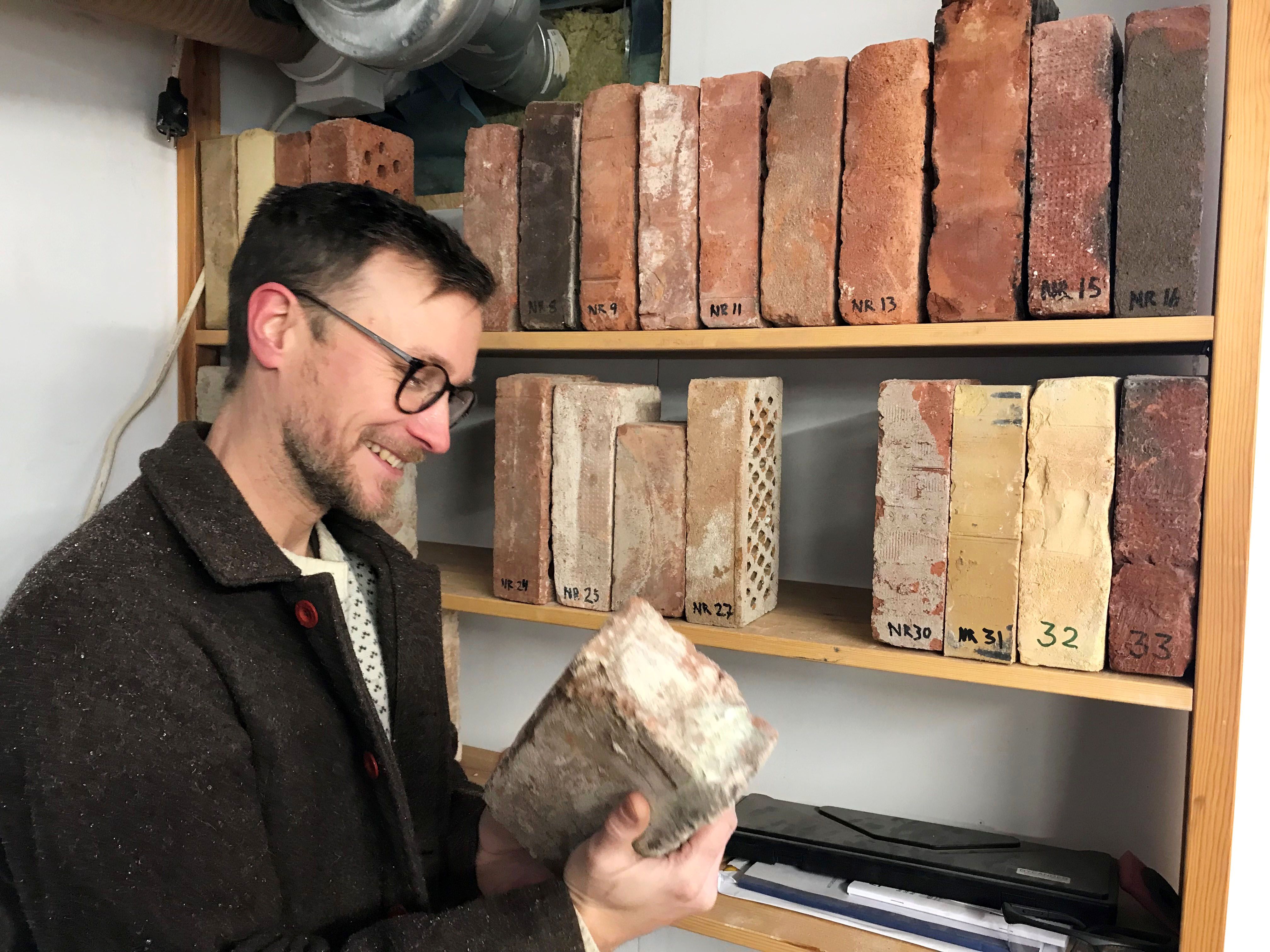 Carl tittar på en tegelsten ur sitt tegelstensbibliotek, som är en hylla med olika tegelstenar med nummer på.