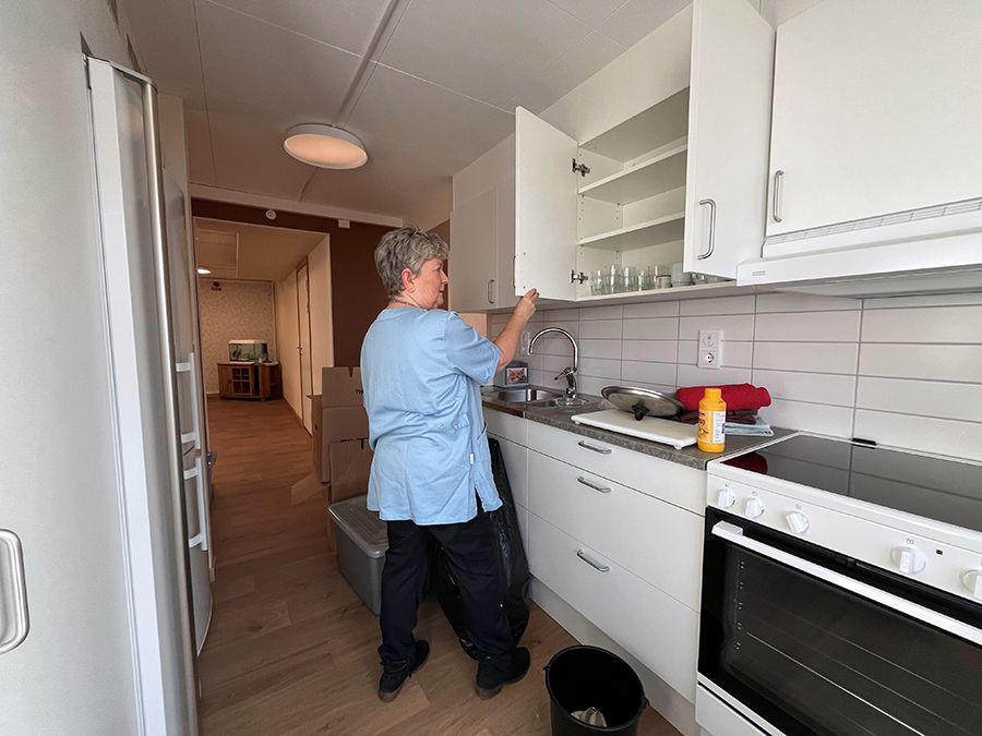 kvinna med kort grått hår och blå arbetströja öppnar en kökslucka.