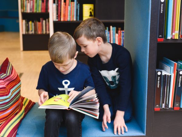 Barn som läser ur en bok i ett bibliotek.
