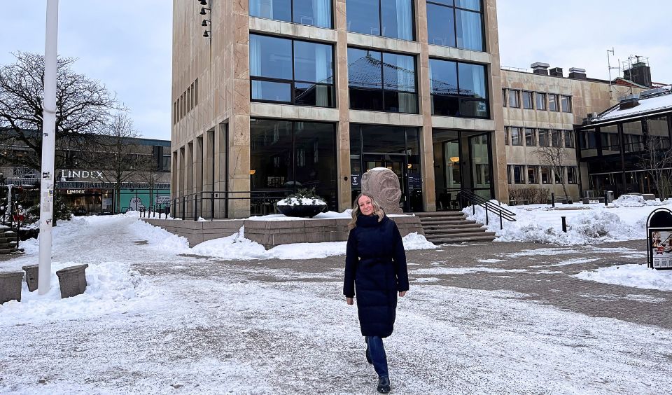 Lotta går  mot kameran, bort från stadshuset. Det är snö. Hon ler och är varmt klädd.