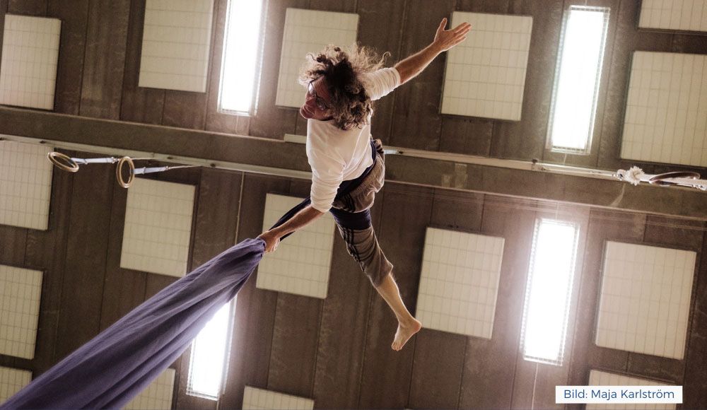 Magnus hänger i tyg från taket (likt trapets). Bild tagen underifrån. Fotograf: Maja Karlström.