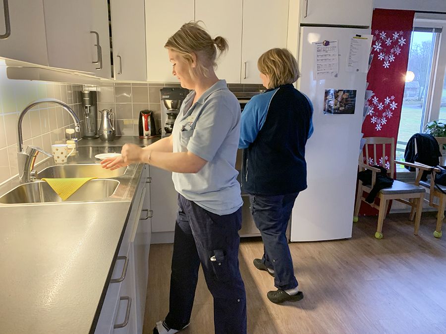 Två kvinnor plockar undan på diskbänken inne i köket på boendet.