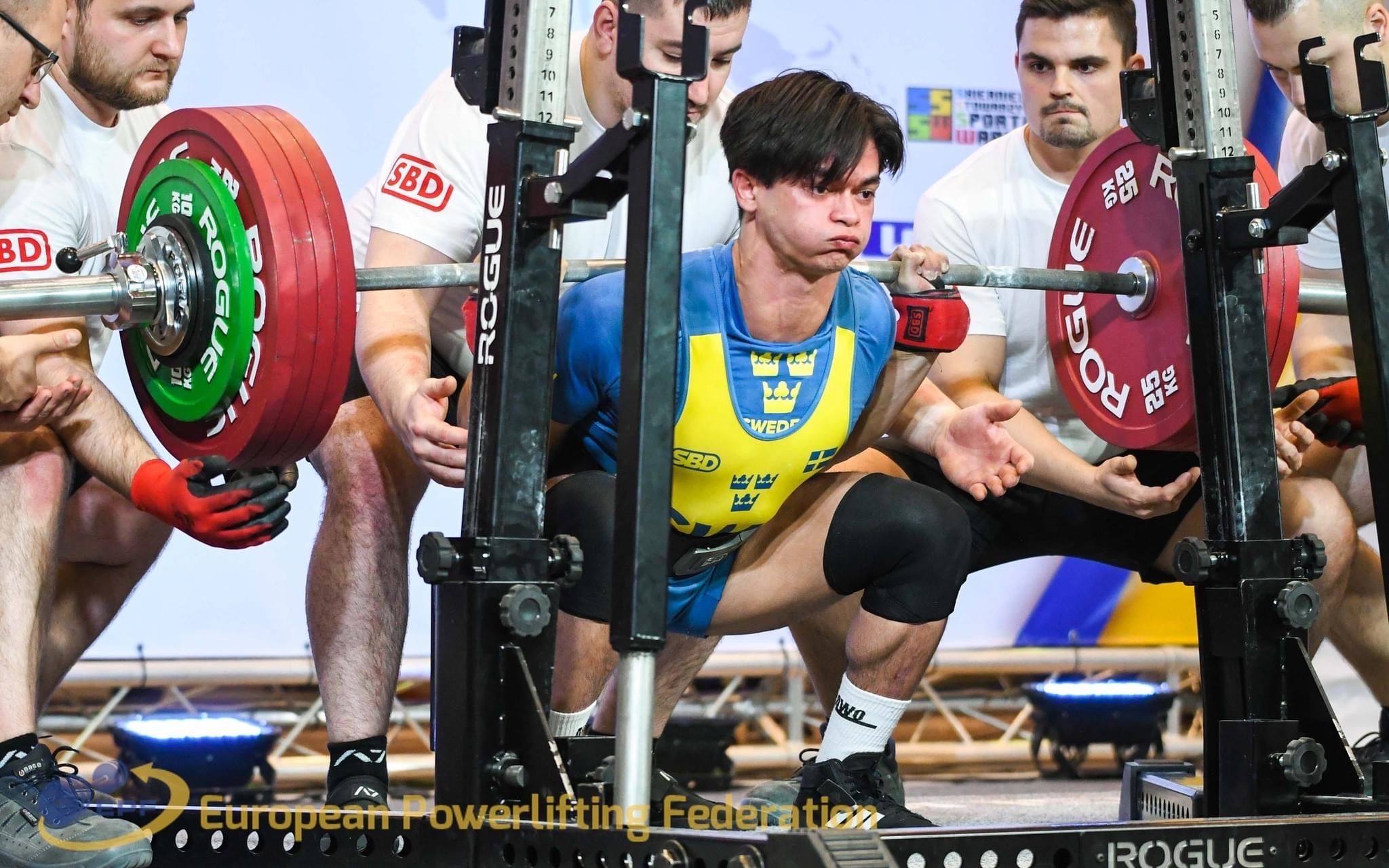 Carl i knäböjd position, håller en skivstång med mycket vikt.