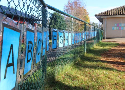 Alfabetsskyltar på staket, förskola med skylt i bakgrunden