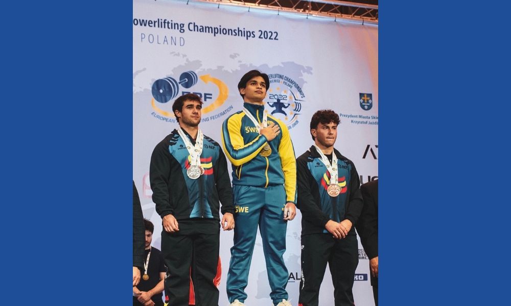 Carl på podium med guldmedalj och hand över bröstet. Silver och bronsmedaljör bredvid.