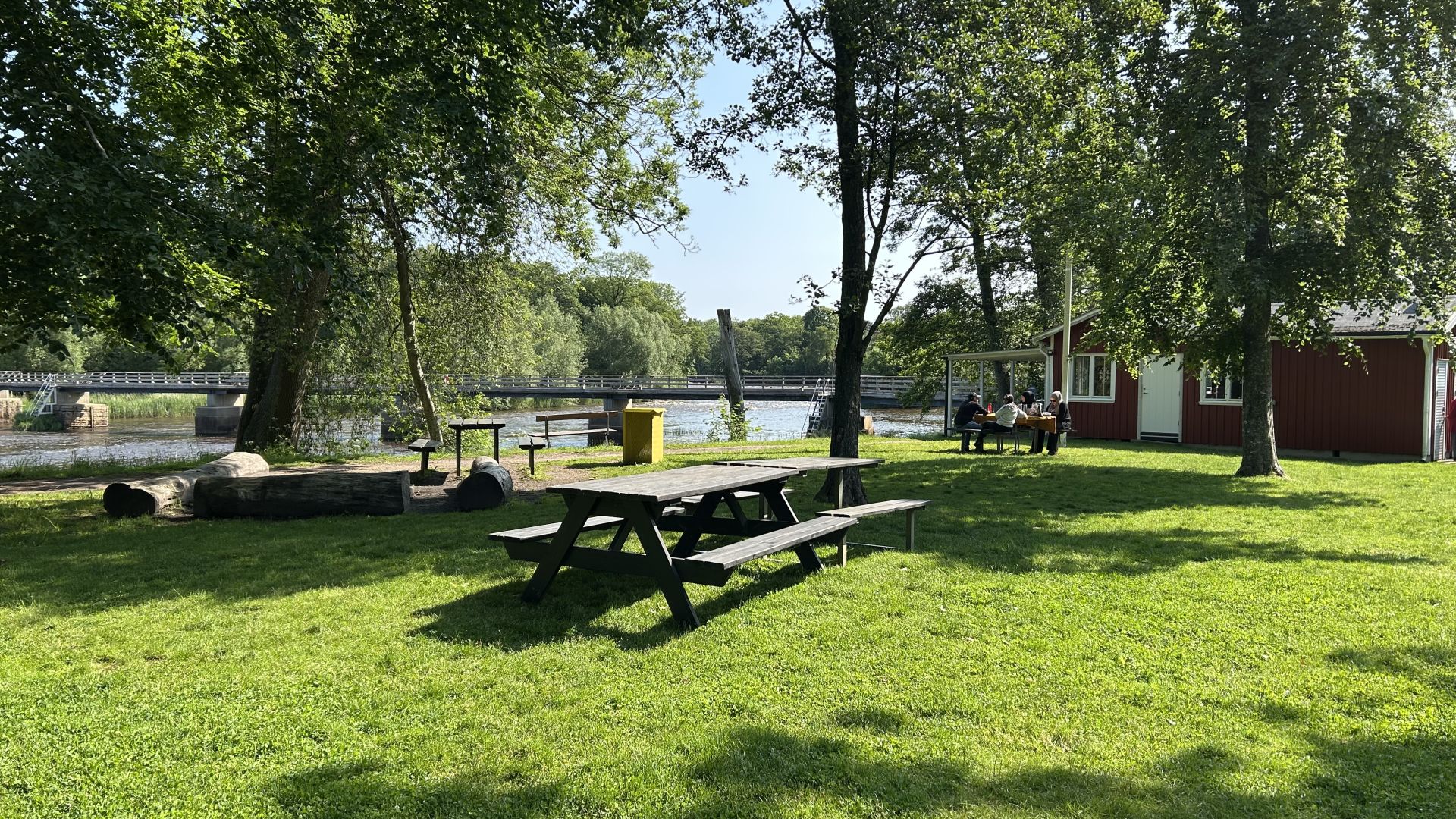 Picknickbord i trä på en gräsmatta med ett rött trähus i bakgrunden