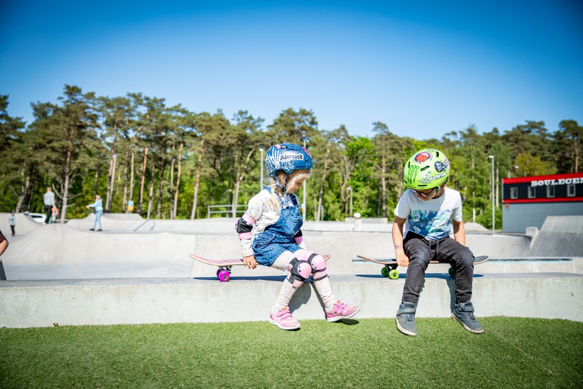 Två barn sitter på sin skateboard vid kanten av skateparken.