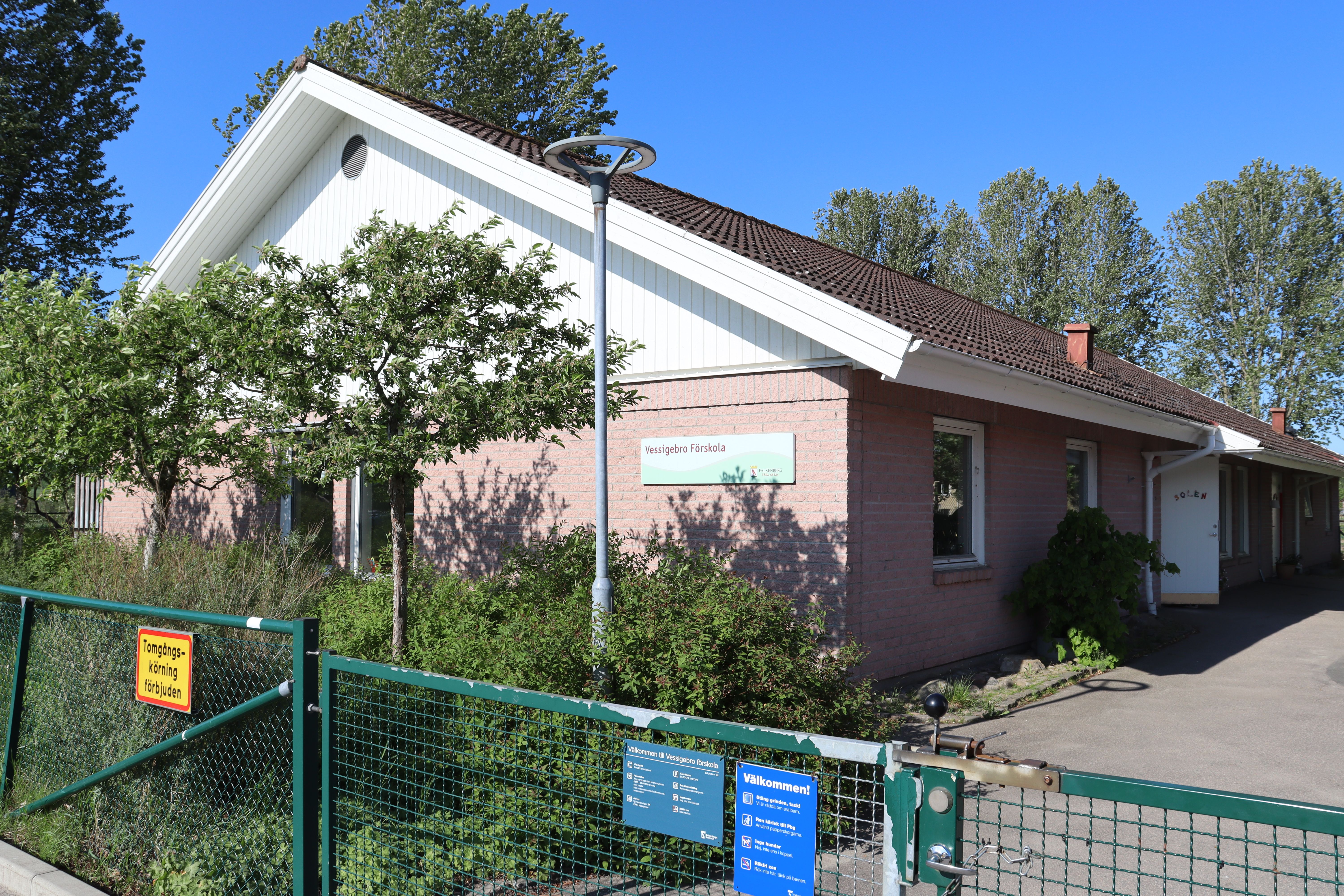 Låg ljusröd och vit byggnad sedd från gaveln, skylt med "Vessigebro förskola" på fasaden