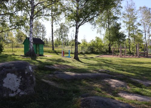 Gräsplan med stenar i förgrunden och träd, balansbana och hinder i bakgrunden