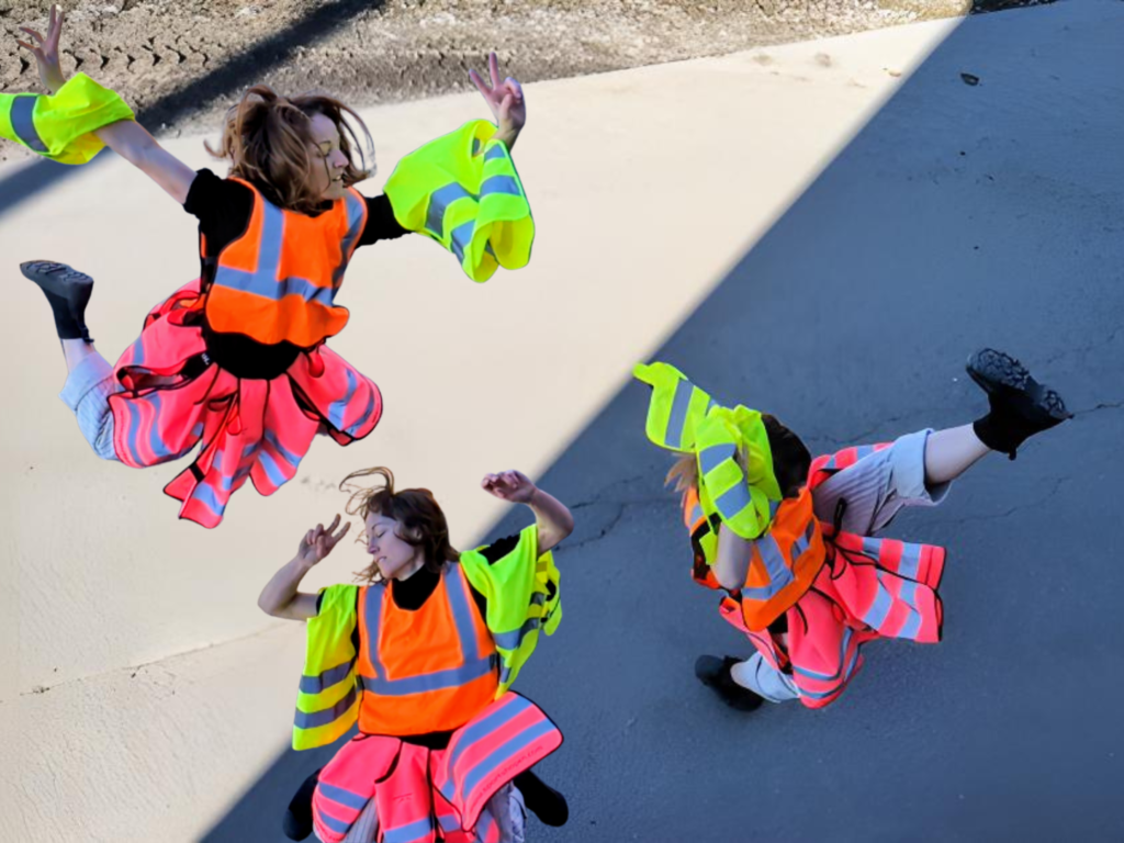 Tre kvinnor dansar klädda i varselvästar i gult, orange och rosa.