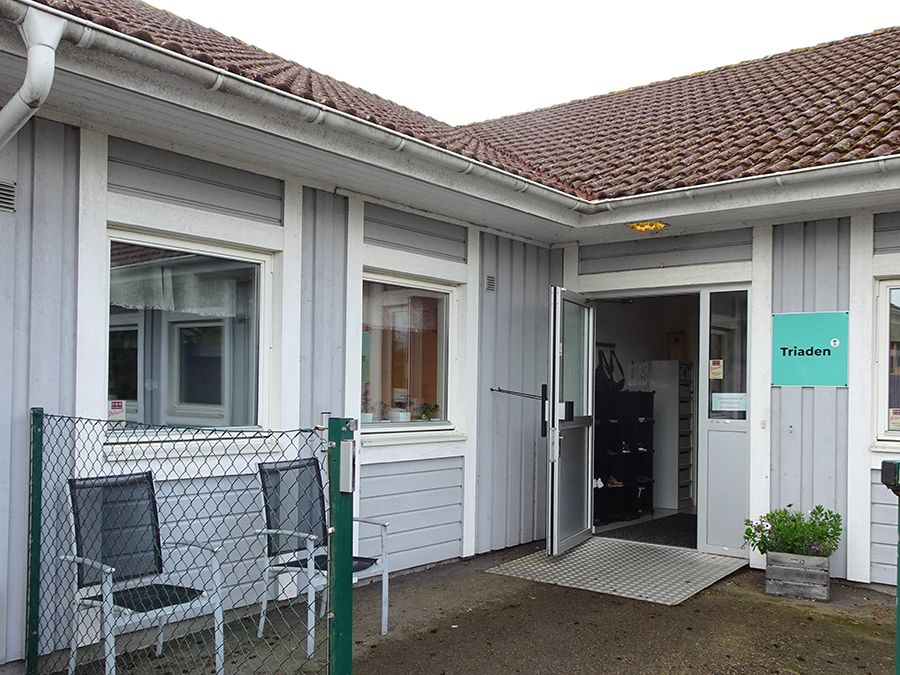 Entrén till ett ljusgrått trähus med vita knutar.