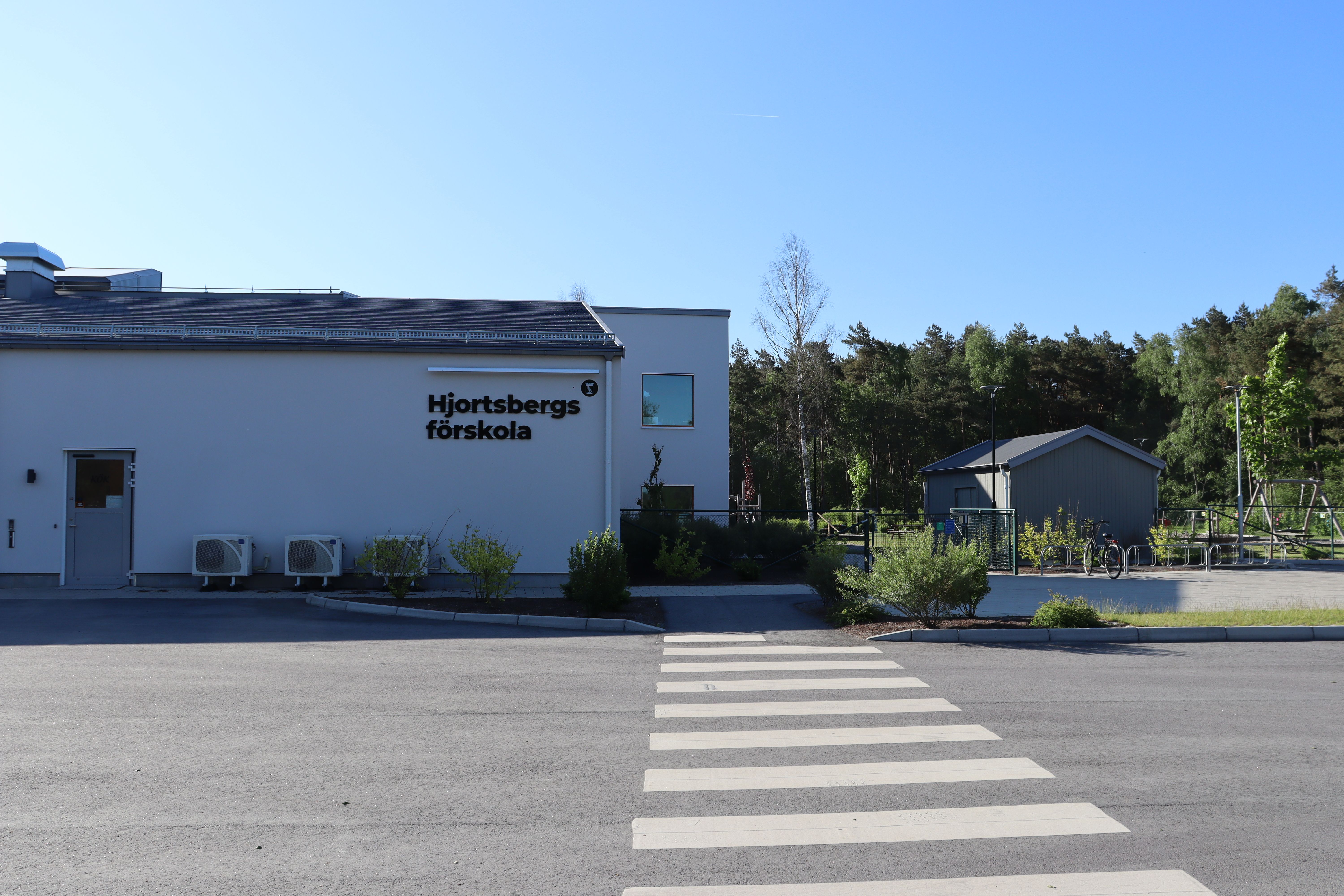 Låg vit byggnad med Hjortsbergs förskola på fasaden, övergångsställe i förgrunden